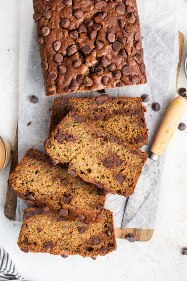 A loaf of zucchini banana bread on a wooden cutting board with four slices cut from it.