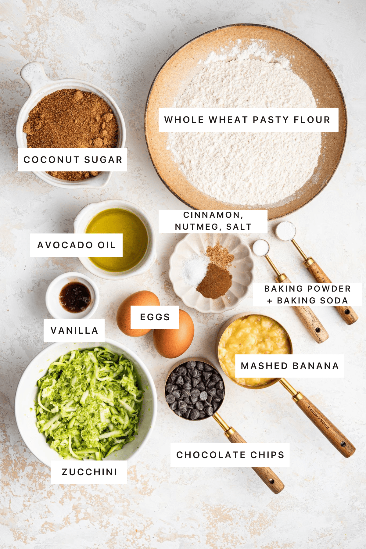 Ingredients for zucchini banana bread: whole wheat pastry flour, coconut sugar, cinnamon, nutmeg, salt, baking powder, baking soda, mashed banana, zucchini, eggs, vanilla, avocado oil and chocolate chips.