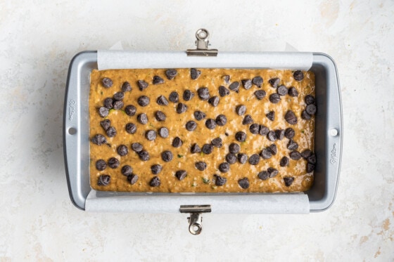 Zucchini banana bread batter in a bread pan before being baked, with many chocolate chips on top.