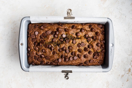 A loaf of zucchini banana bread in a bread pan after being baked, with many chocolate chips on top.