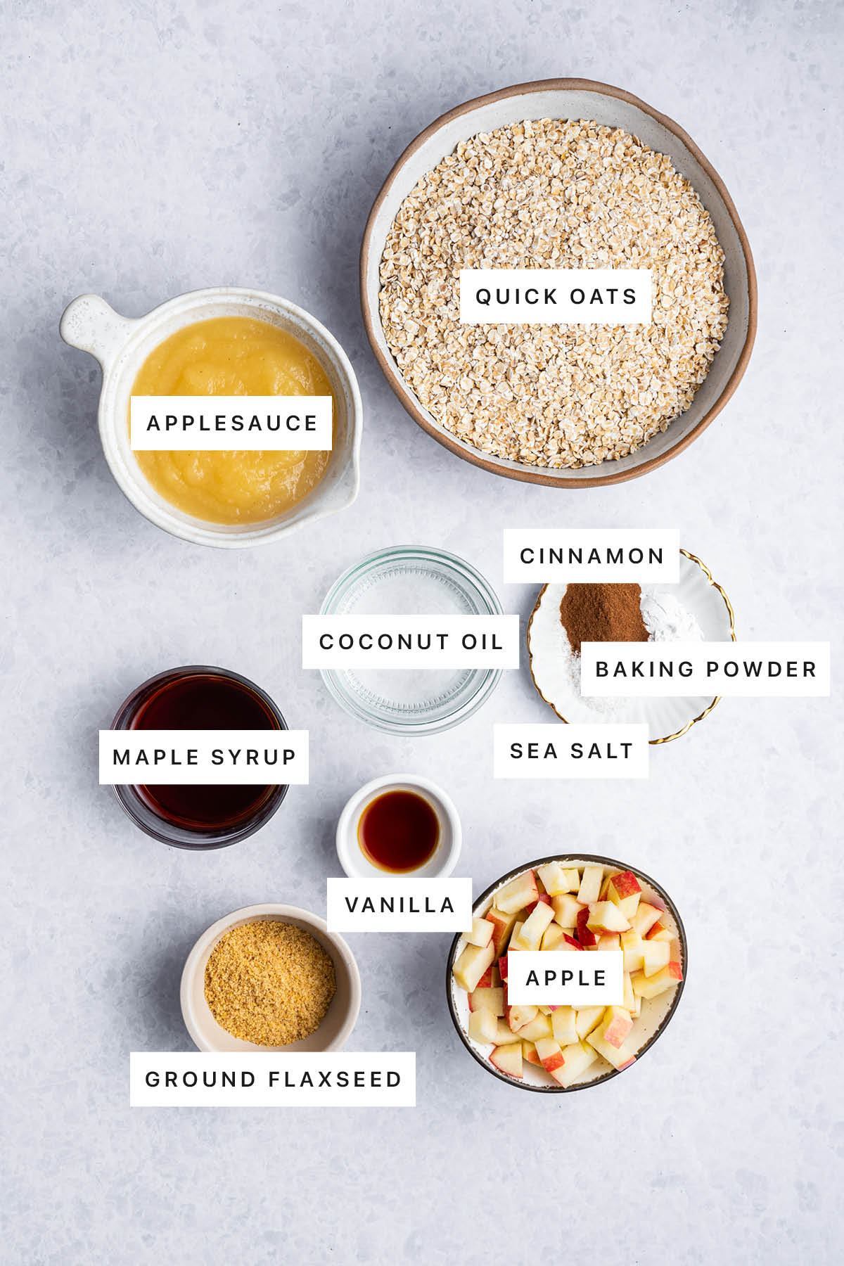 Ingredients measured out to make Apple Oatmeal Bars: applesauce, quick oats, coconut oil, cinnamon, baking powder, sea salt, maple syrup, vanilla, ground flaxseed and apple.
