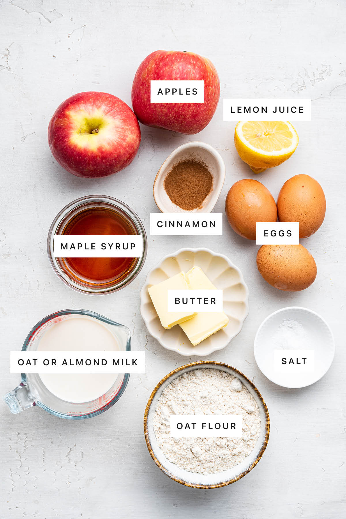 Ingredients measured out to make Apple Dutch Baby: apples, lemon juice, cinnamon, eggs, maple syrup, butter, salt, oat milk and oat flour.