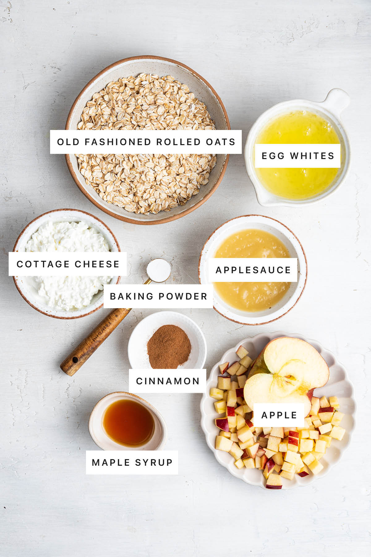 Ingredients measured out to make Healthy Apple Pancakes: oats, egg whites, cottage cheese, applesauce, baking powder, cinnamon, maple syrup and apple.