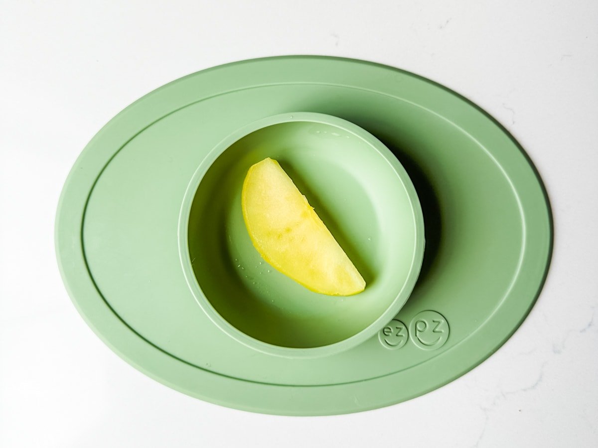 A steamed apple slice in a green ezpz baby bowl.