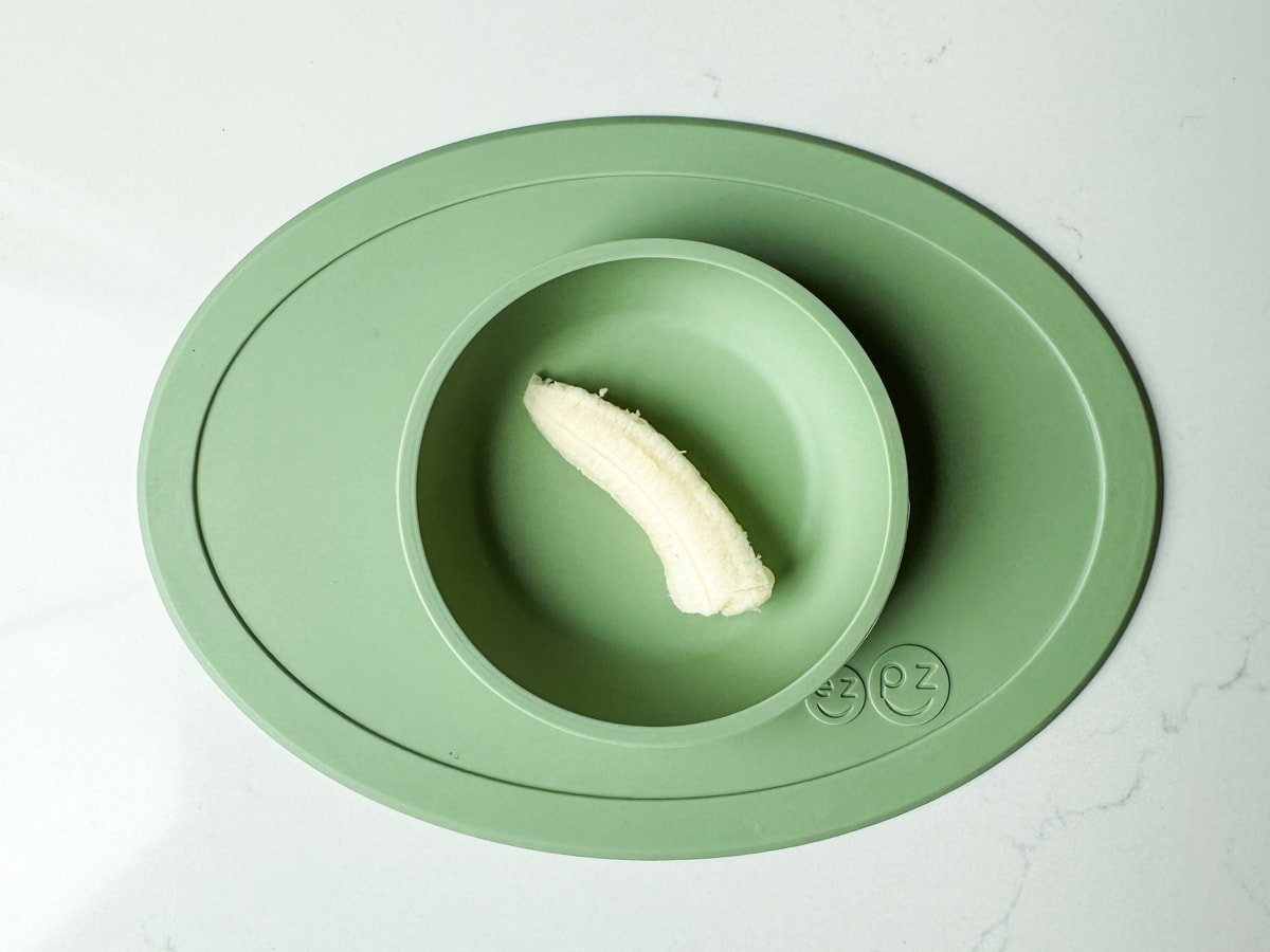 A piece of a banana in a green ezpz baby bowl.