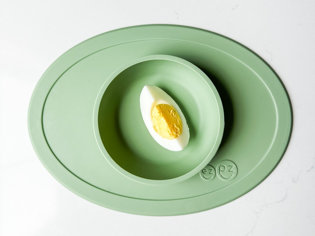 A piece of hard boiled egg in a green ezpz baby bowl.