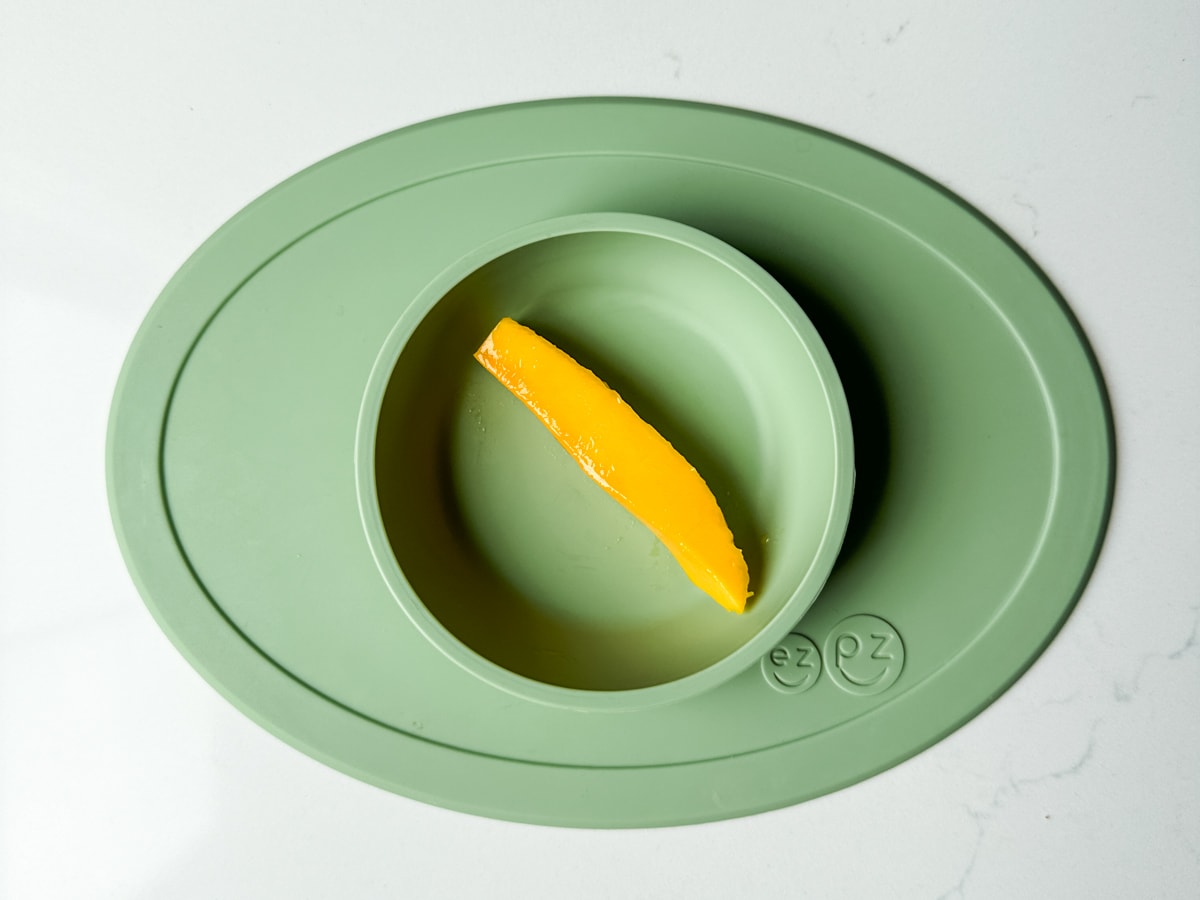 A slice of mango in a green ezpz baby bowl.