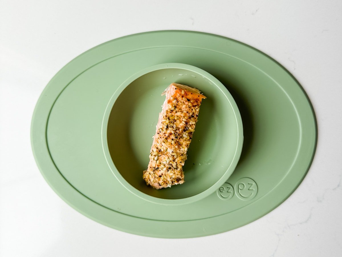 A piece of salmon with seasoning in a green ezpz baby bowl.