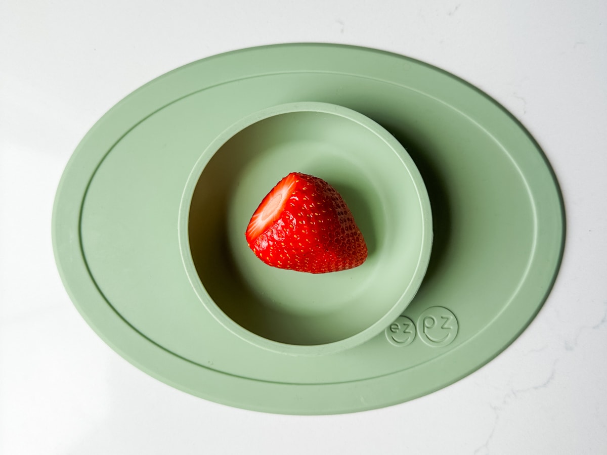 A strawberry in a green ezpz baby bowl.