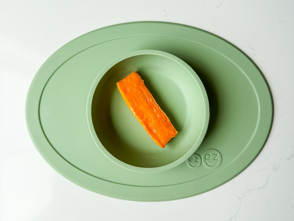 A piece of roasted sweet potato in a green ezpz baby bowl.