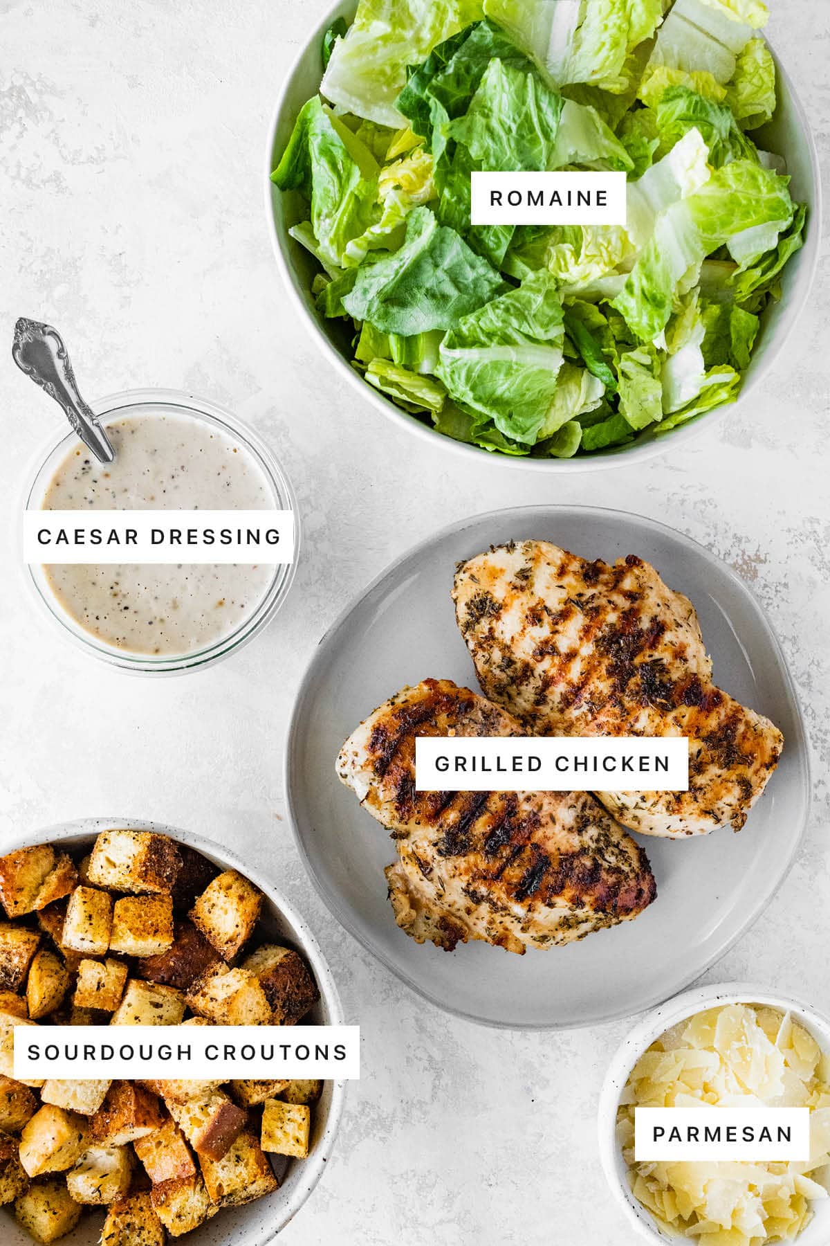 Measured ingredients for Grilled Chicken Caesar Salad: Romaine lettuce, Caesar dressing, grilled chicken, sourdough croutons, and Parmesan.
