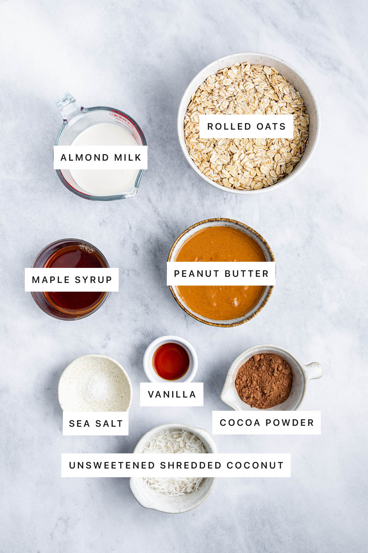 Ingredients measured out to make Healthy No Bake Chocolate Coconut Bars: almond milk, rolled oats, maple syrup, peanut butter, sea salt, vanilla, cocoa powder and shredded coconut.