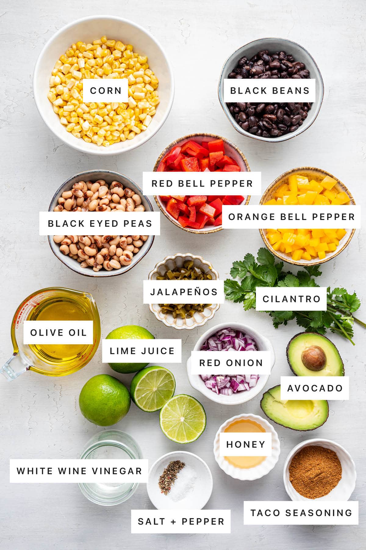 Ingredients measured out to make Cowboy Caviar: corn, black beans, bell pepper, black eyes peas, jalapeños, olive oil, lime, cilantro, red onion, avocado, honey, white wine vinegar, salt, pepper and taco seasoning.