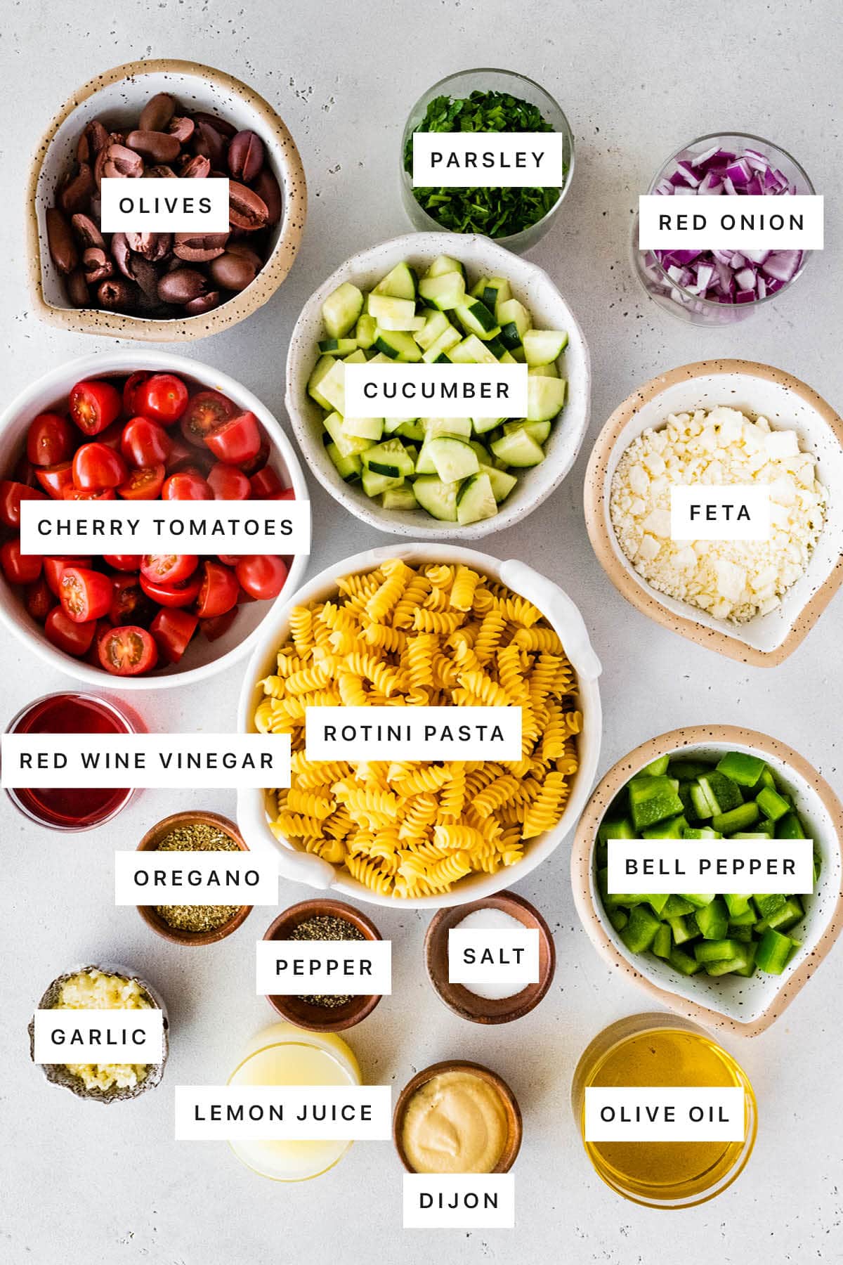 Ingredients for the Greek pasta salad: kalamata olives, cherry tomatoes, cucumbers, parsley, red onion, feta cheese, pasta, green bell pepper, red wine vinegar, dried oregano, salt, pepper, olive oil, garlic, lemon juice and dijon mustard.