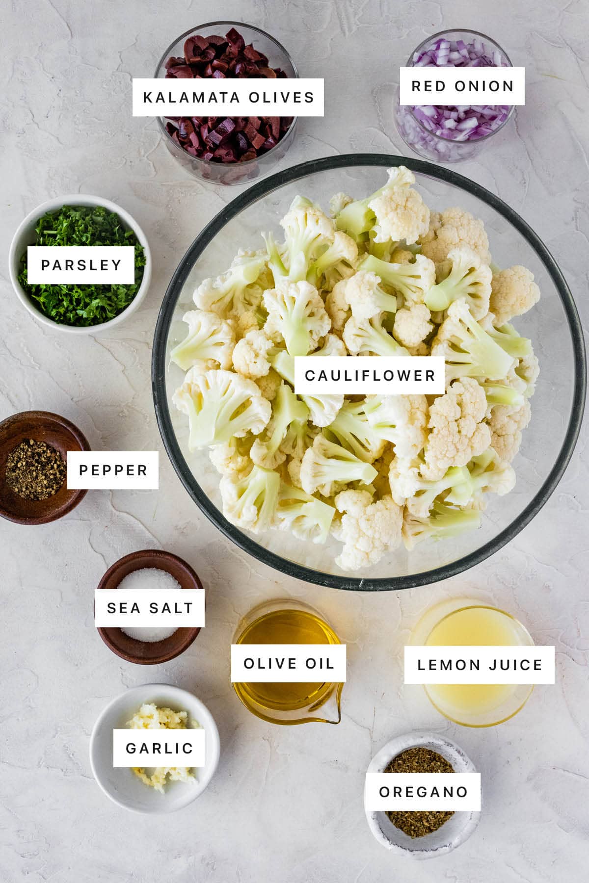 Measured ingredients to make Roasted Cauliflower Salad: kalamata olives, red onion, parsley, cauliflower, pepper, sea salt, olive oil, lemon juice, garlic, and oregano.