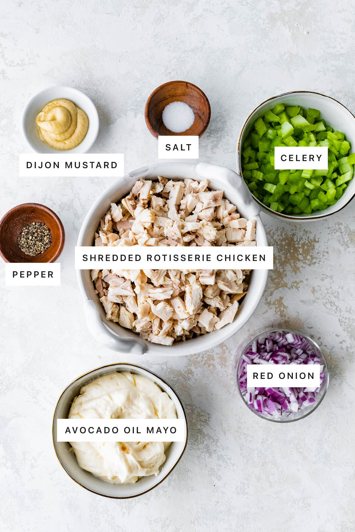 Ingredients measured out to make Rotisserie Chicken Salad: dijon mustard, salt, celery, pepper, shredded rotisserie chicken, avocado oil mayo and red onion.