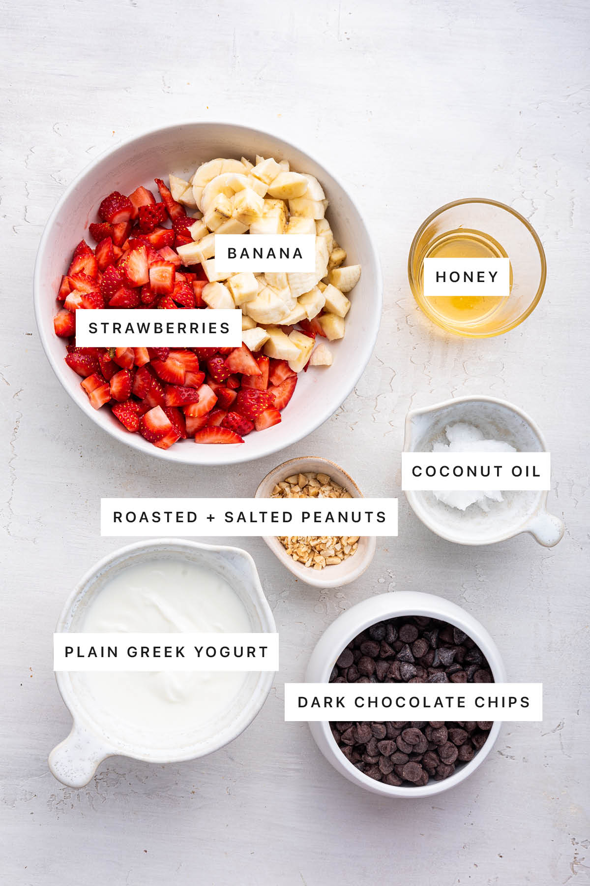 Ingredients measured out to make Chocolate Strawberry Banana Yogurt Clusters: banana, strawberry, honey, peanuts, coconut oil, Greek yogurt and chocolate chips.