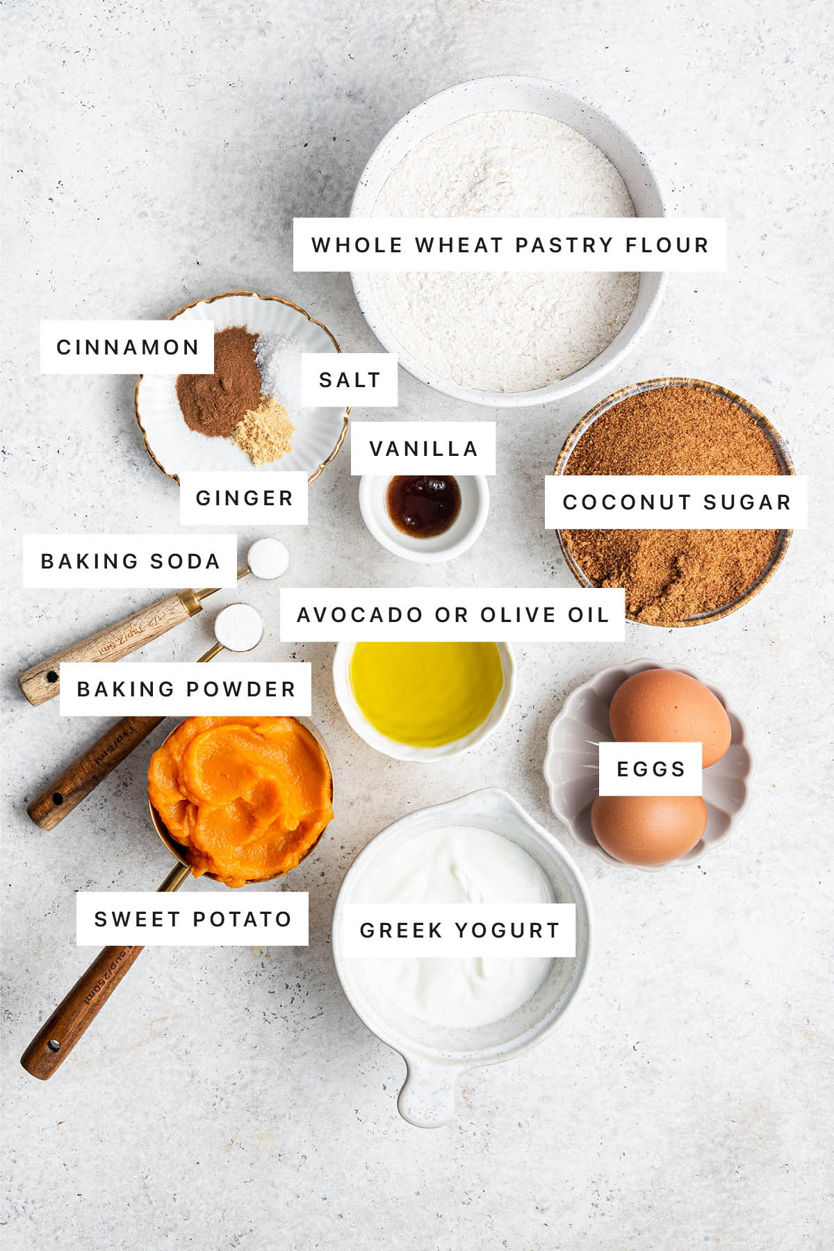 Ingredients measured out to make Healthy Sweet Potato Muffins: whole wheat pastry flour, cinnamon, salt, vanilla, ginger, coconut sugar, baking soda, baking powder, avocado/olive oil, eggs, sweet potato and Greek yogurt.