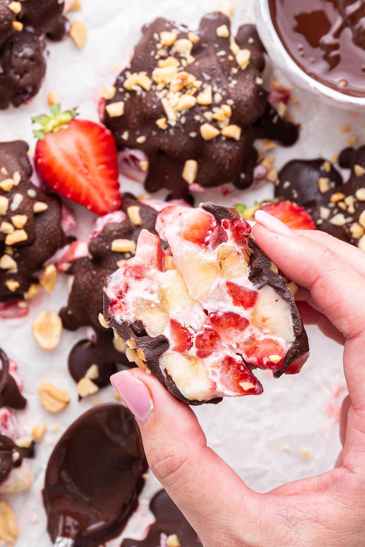A woman's hand holding a chocolate strawberry banana yogurt cluster that is split in half.