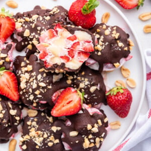Chocolate strawberry banana yogurt clusters on a white plate with one of them split in half to see the inside of the cluster.