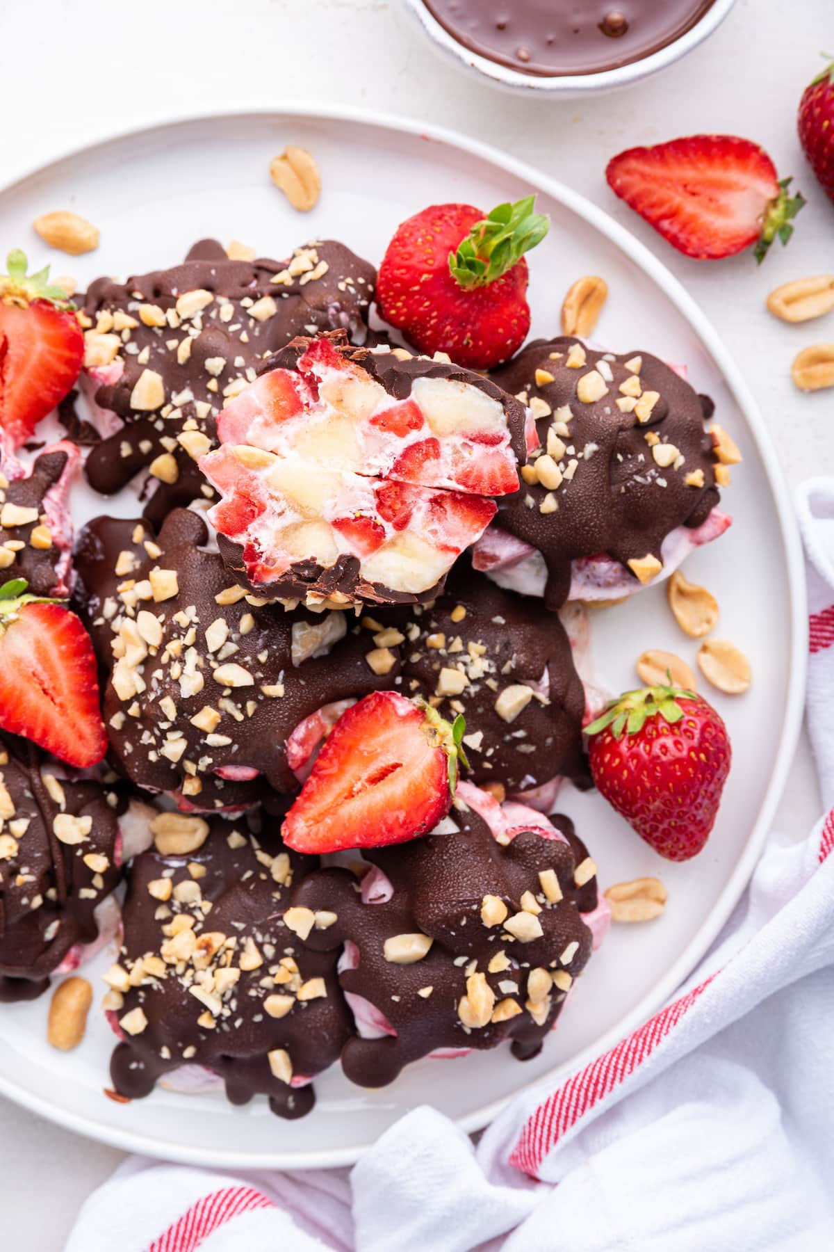 Chocolate strawberry banana yogurt clusters on a white plate with one of them split in half to see the inside of the cluster.