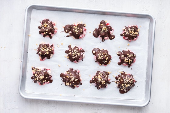 Twelve chocolate strawberry banana yogurt clusters with peanuts on top, on a baking tray.