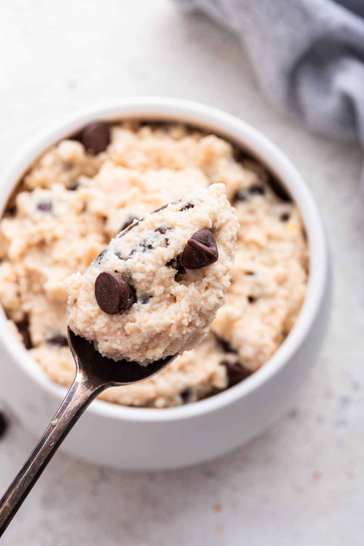 A spoon holding a scoop of cottage cheese cookie dough over a bowl full of dough.