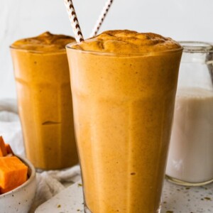 Two glasses with a sweet potato smoothie, straws, and topped off with ground cinnamon.