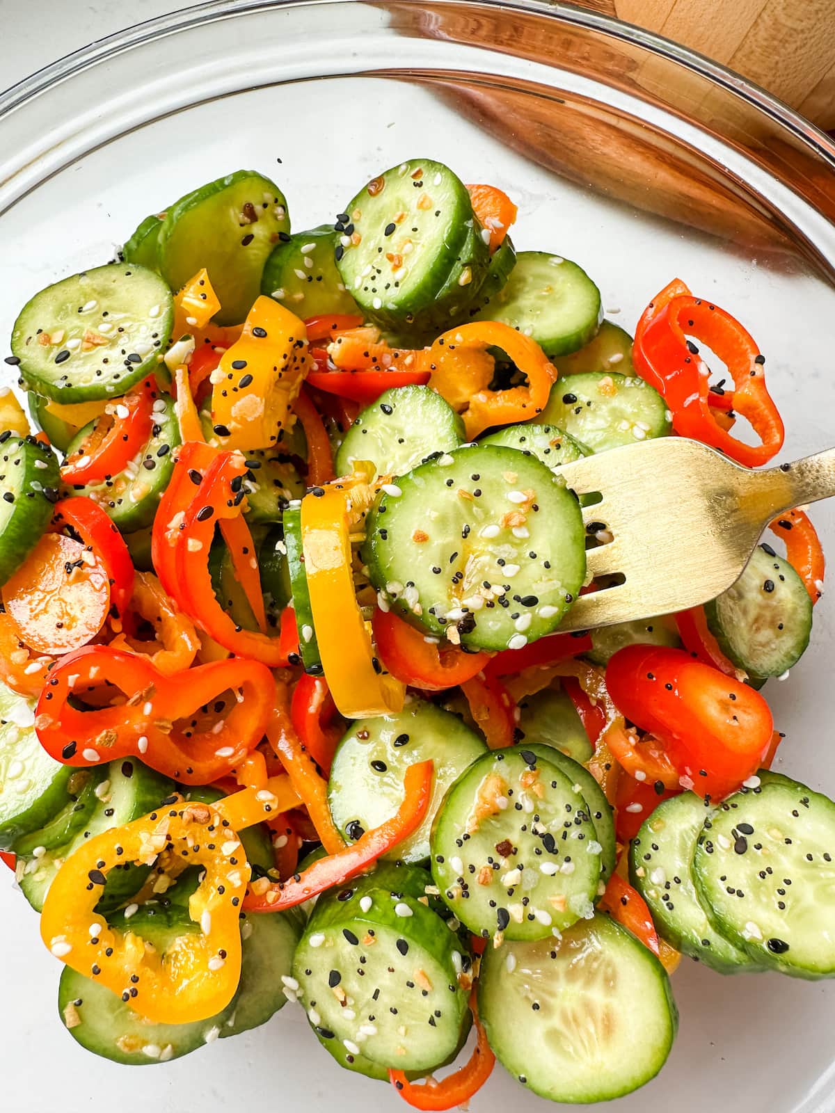 Cucumber and bell pepper salad in a clear mixing bowl with a gold fork.