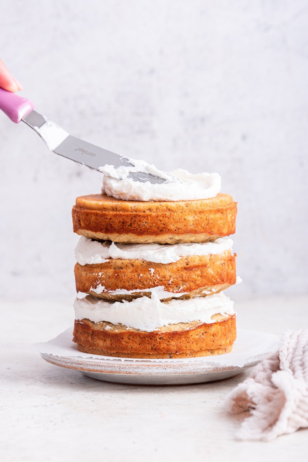 A woman's hand spreading the frosting onto the 3-layer smash cake.