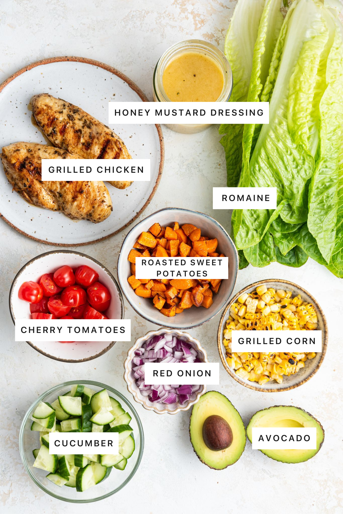 Ingredients measured out to make a Grilled Chicken Salad: grilled chicken, honey mustard dressing, romaine, roasted sweet potatoes, cherry tomatoes, grilled corn, red onion, cucumber and avocado.