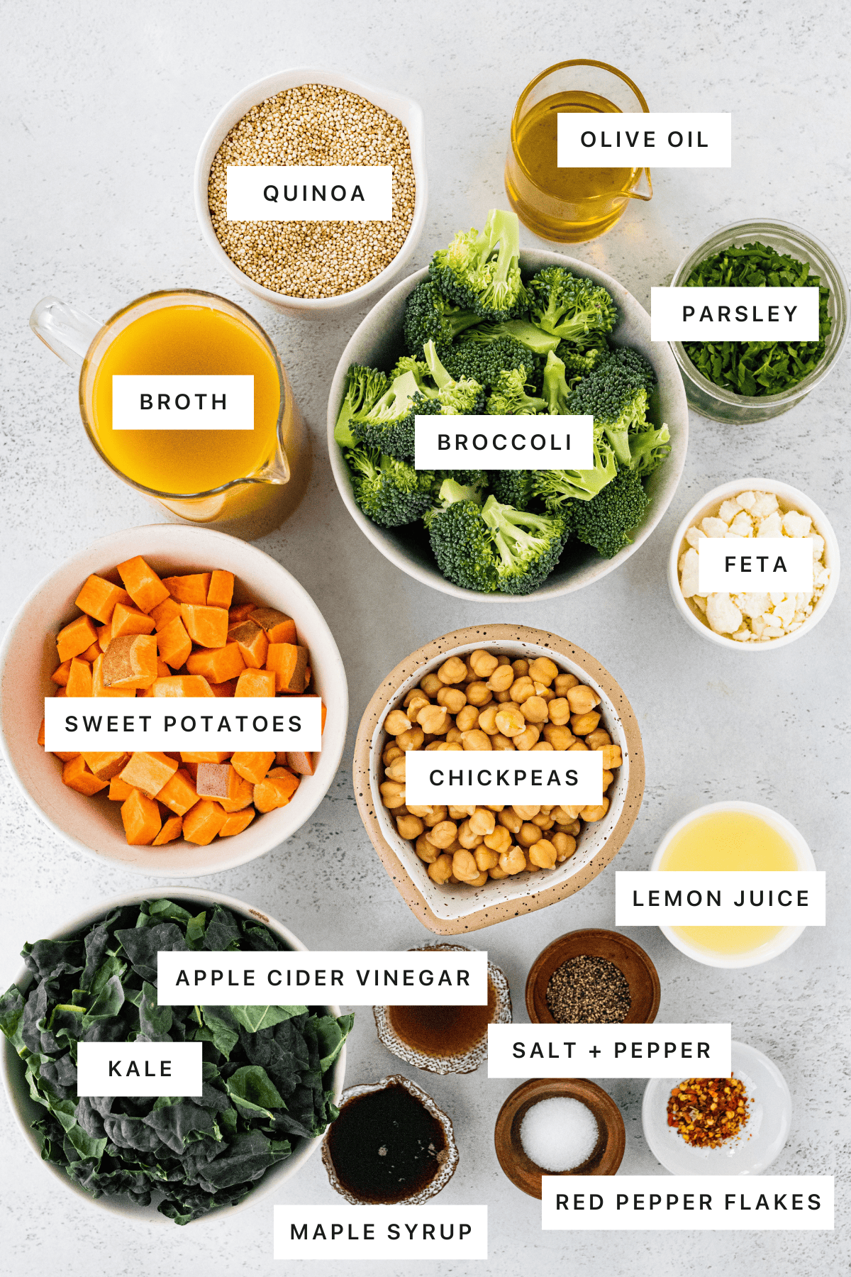 Ingredients measured out to make Roasted Broccoli Quinoa Salad: quinoa, olive oil, parsley, broth, broccoli, feta, sweet potatoes, chickpeas, lemon juice, apple cider vinegar, kale, salt, pepper, maple syrup and red pepper flakes.