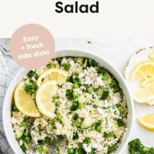 Lemon orzo salad with fresh lemon slices in a white bowl with metal serving spoons.