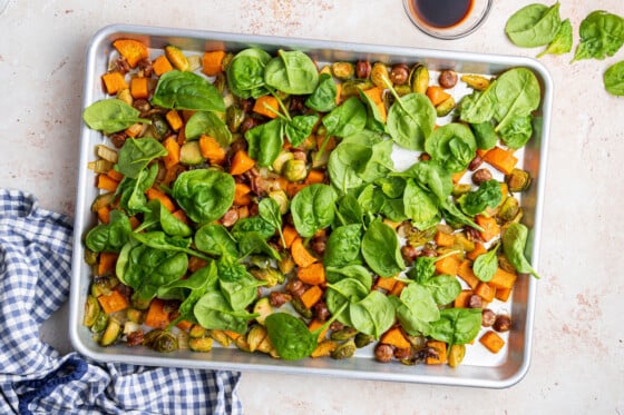 Spinach on top of the vegetables and sausage on a baking tray for the sweet potato hash.