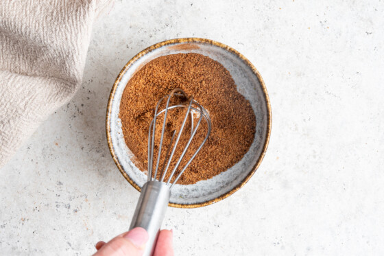 A woman's hand using a metal whisk in a small bowl of cinnamon and sugar.