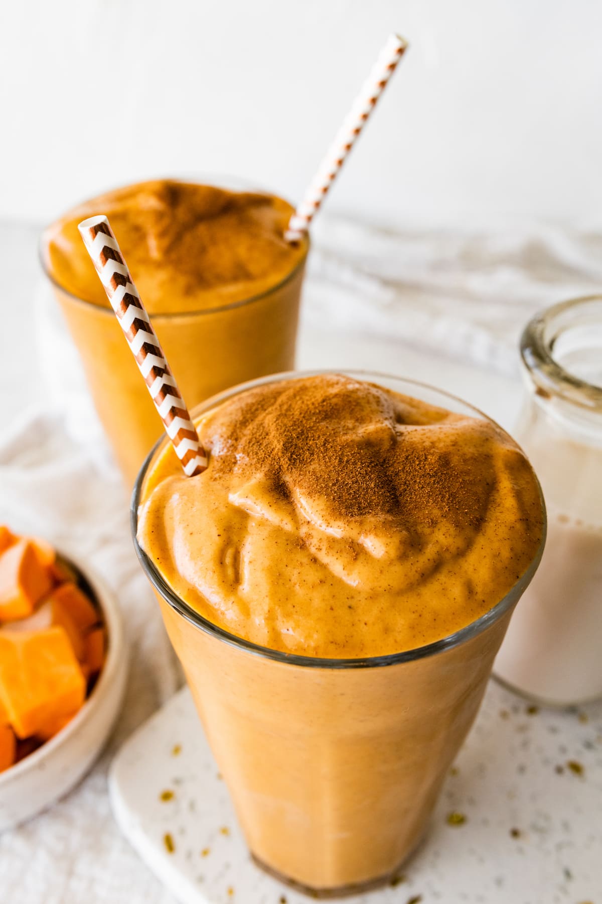 Two glasses with a sweet potato smoothie, straws, and topped off with ground cinnamon.