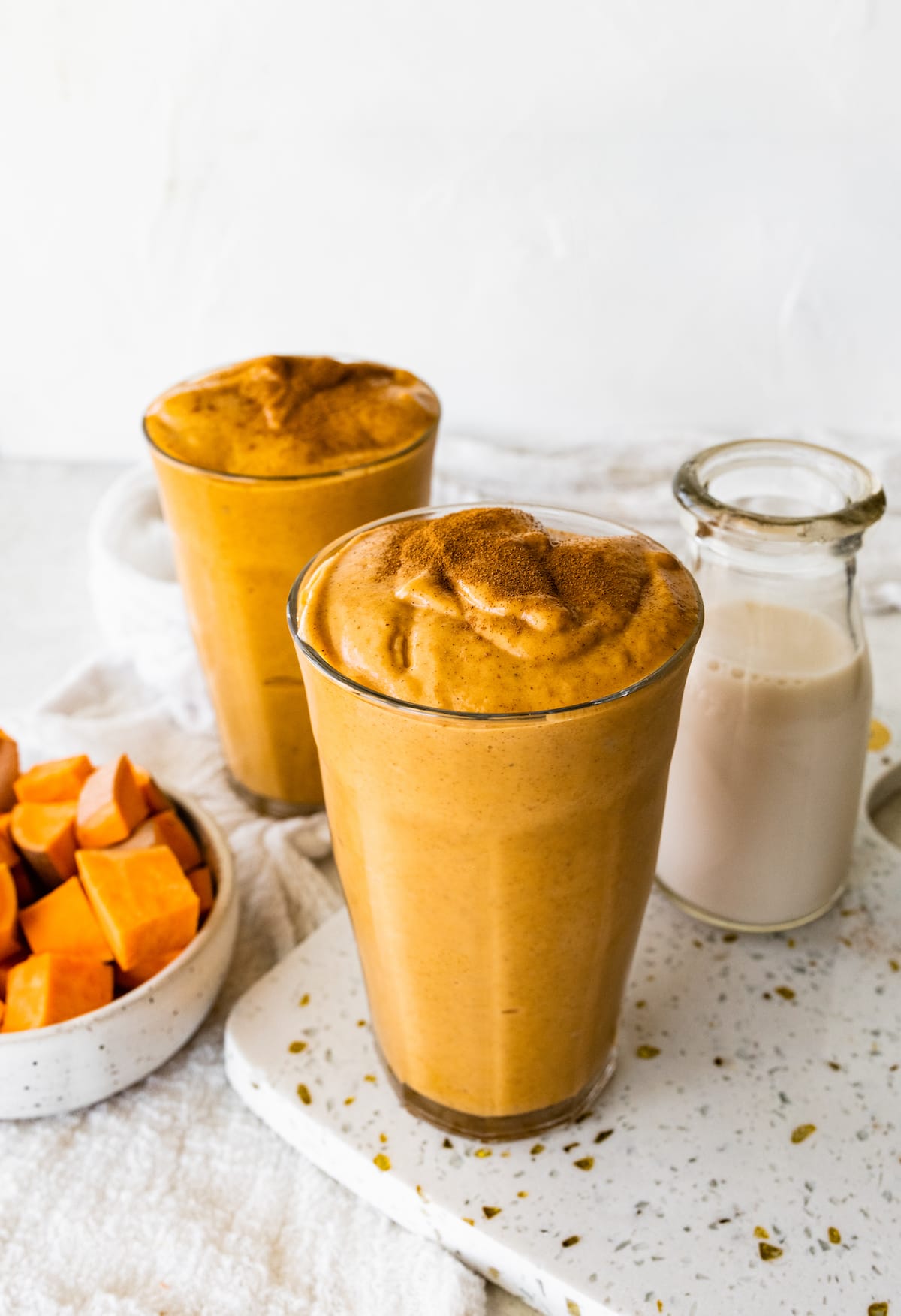 Two glasses with sweet potato smoothies and topped off with ground cinnamon.