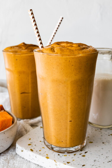 Two glasses with a sweet potato smoothie, straws, and topped off with ground cinnamon.