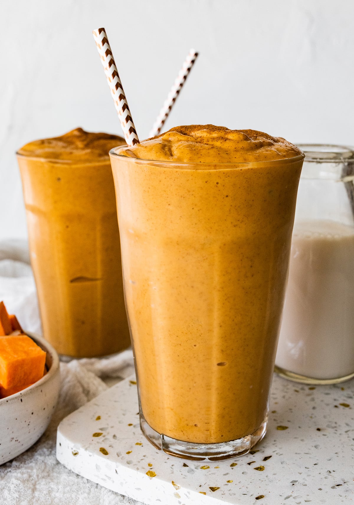 Two glasses with a sweet potato smoothie, straws, and topped off with ground cinnamon.
