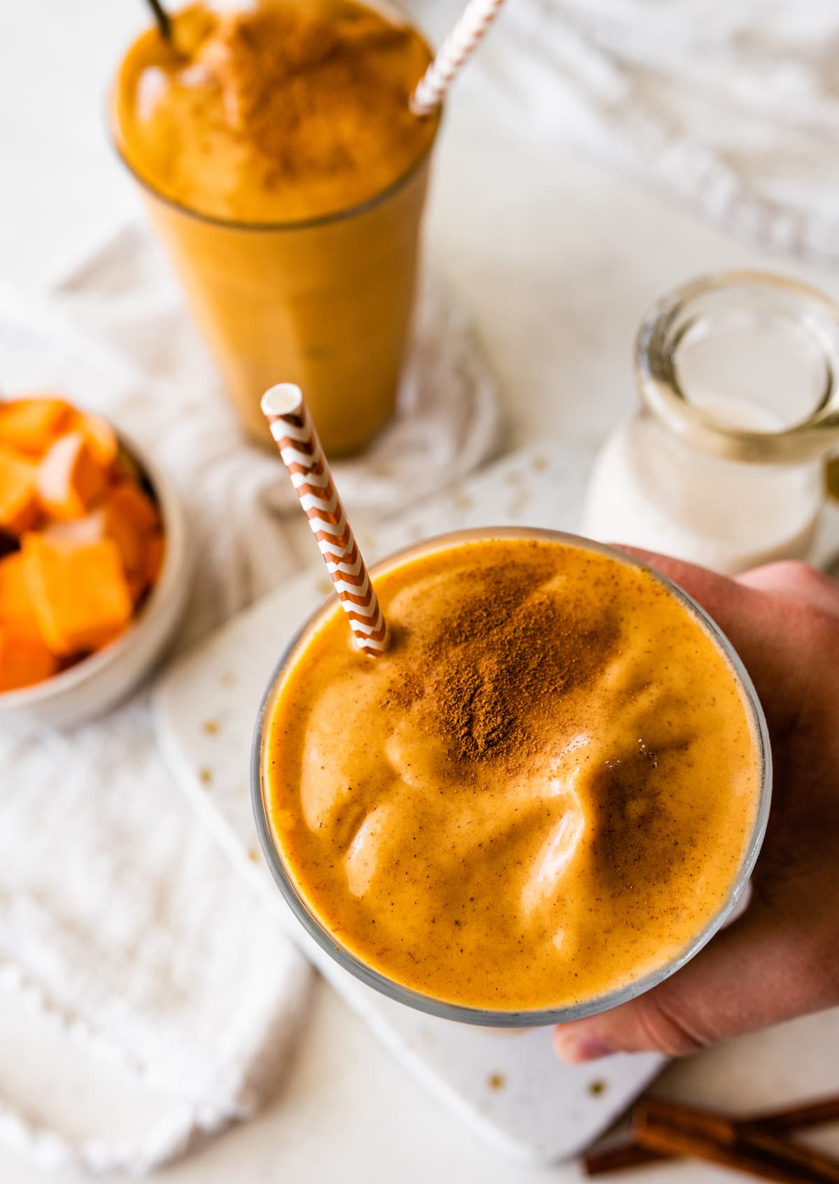 A hand holding a glass of a sweet potato smoothie topped with ground cinnamon.