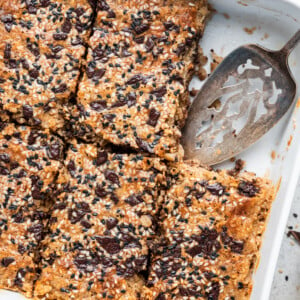 Tahini baked oatmeal in a square baking dish with a metal serving spatula and a piece missing.