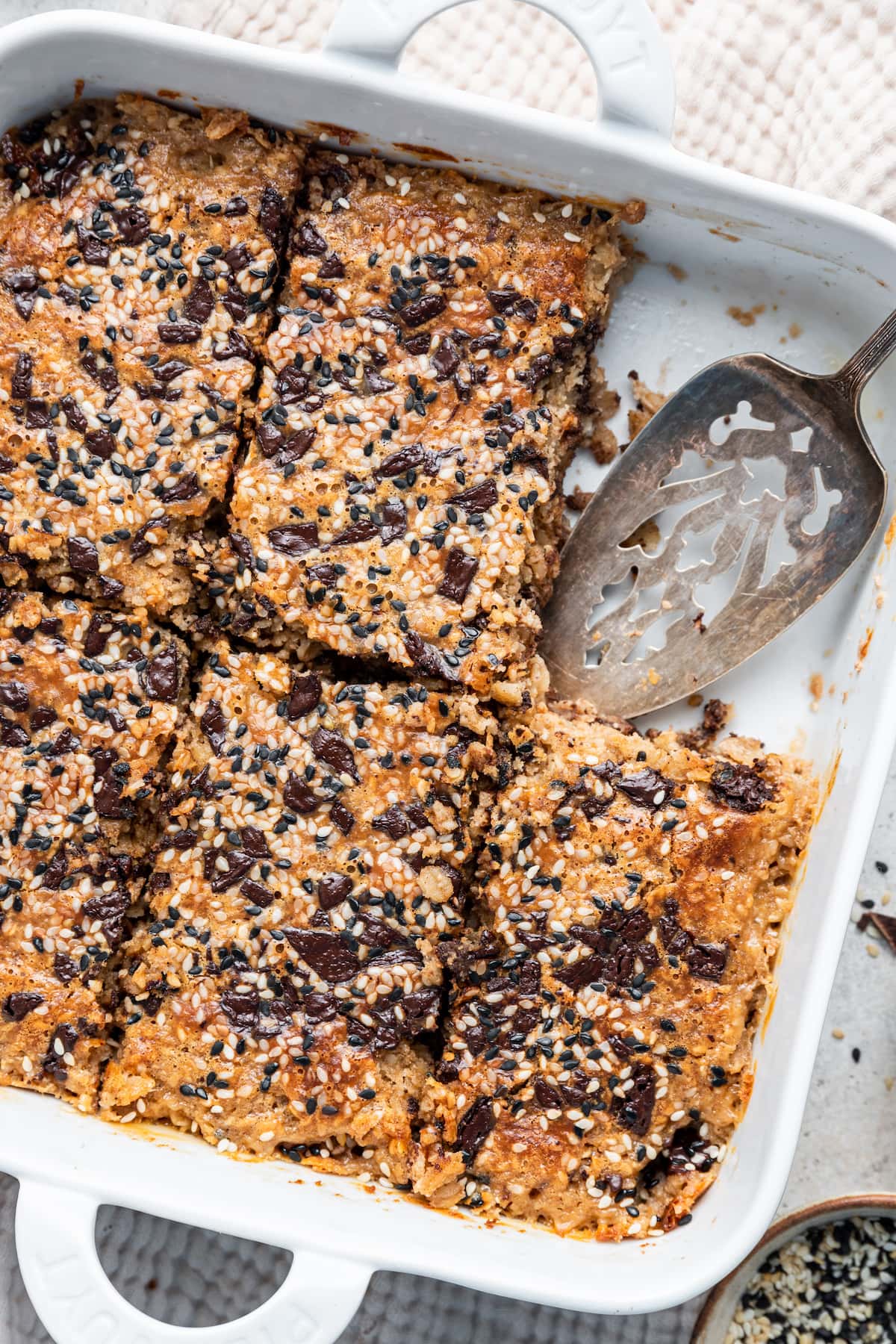 Tahini baked oatmeal in a square baking dish with a metal serving spatula and a piece missing.