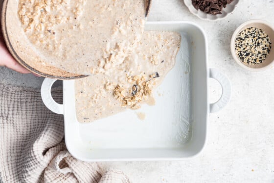 Tahini baked oatmeal mixture being poured into a prepared square baking dish.