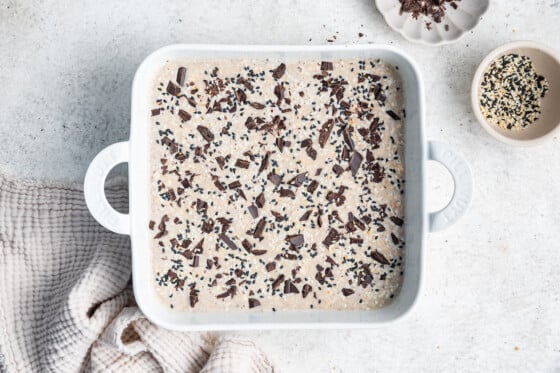 Tahini baked oatmeal topped with chocolate chips in a square baking dish before being baked.