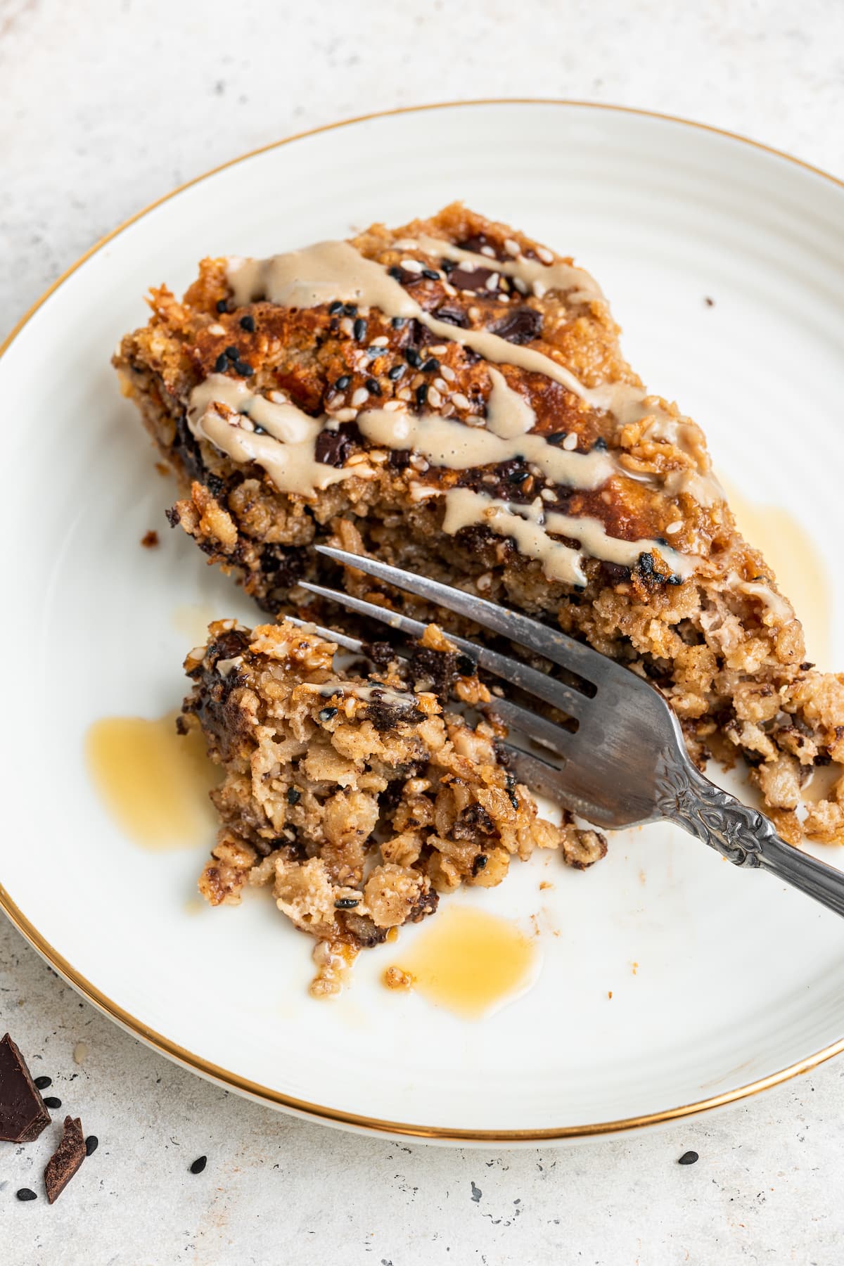 A fork taking a bite size piece from a piece of tahini baked oatmeal on a white plate.