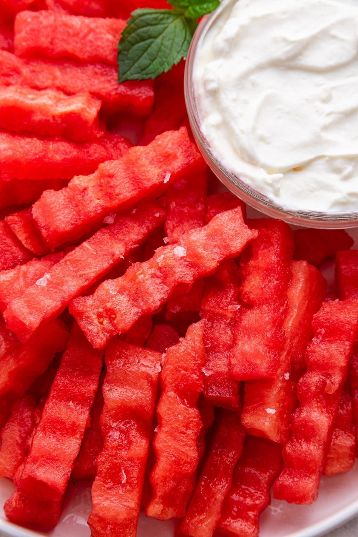 A close up image of watermelon fries on a plate served with a yogurt dip.