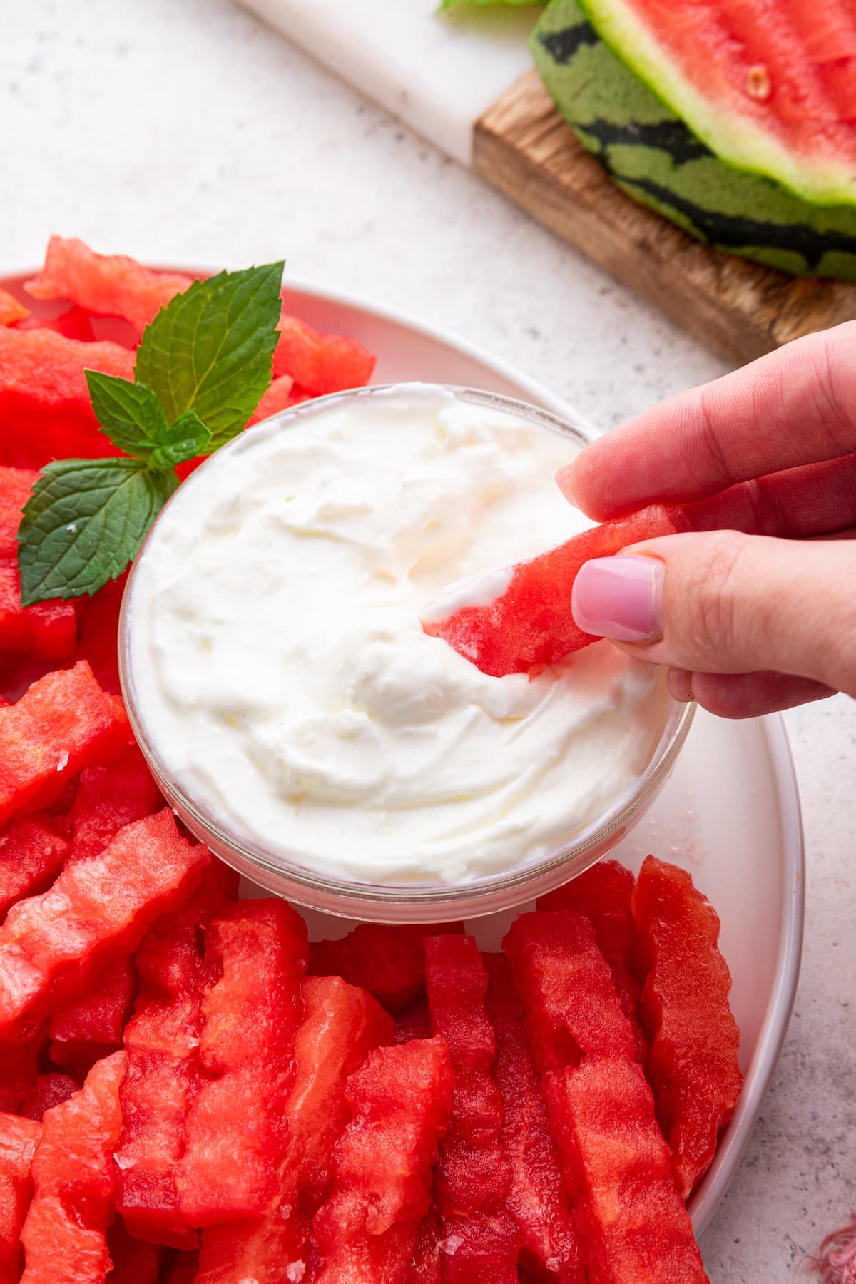 A woman's hand dipping one watermelon fry into a yogurt dip.