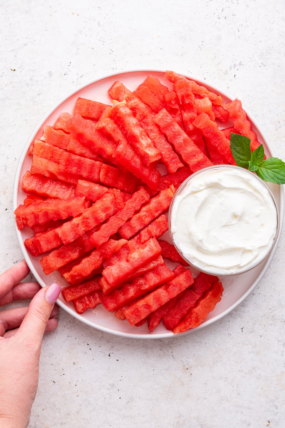 A woman's hand grabbing a plate of watermelon fries served with a yogurt dip.