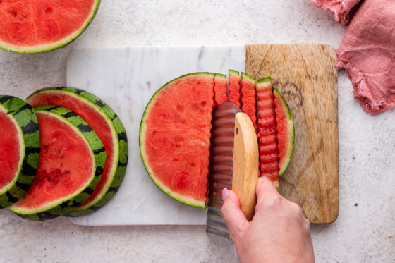 Woman's hand cutting the watermelon with a crinkle cutter.