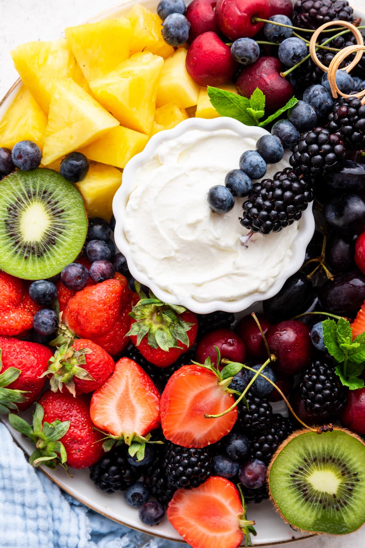 A yogurt fruit dip surrounded by fresh fruit on a white plate.